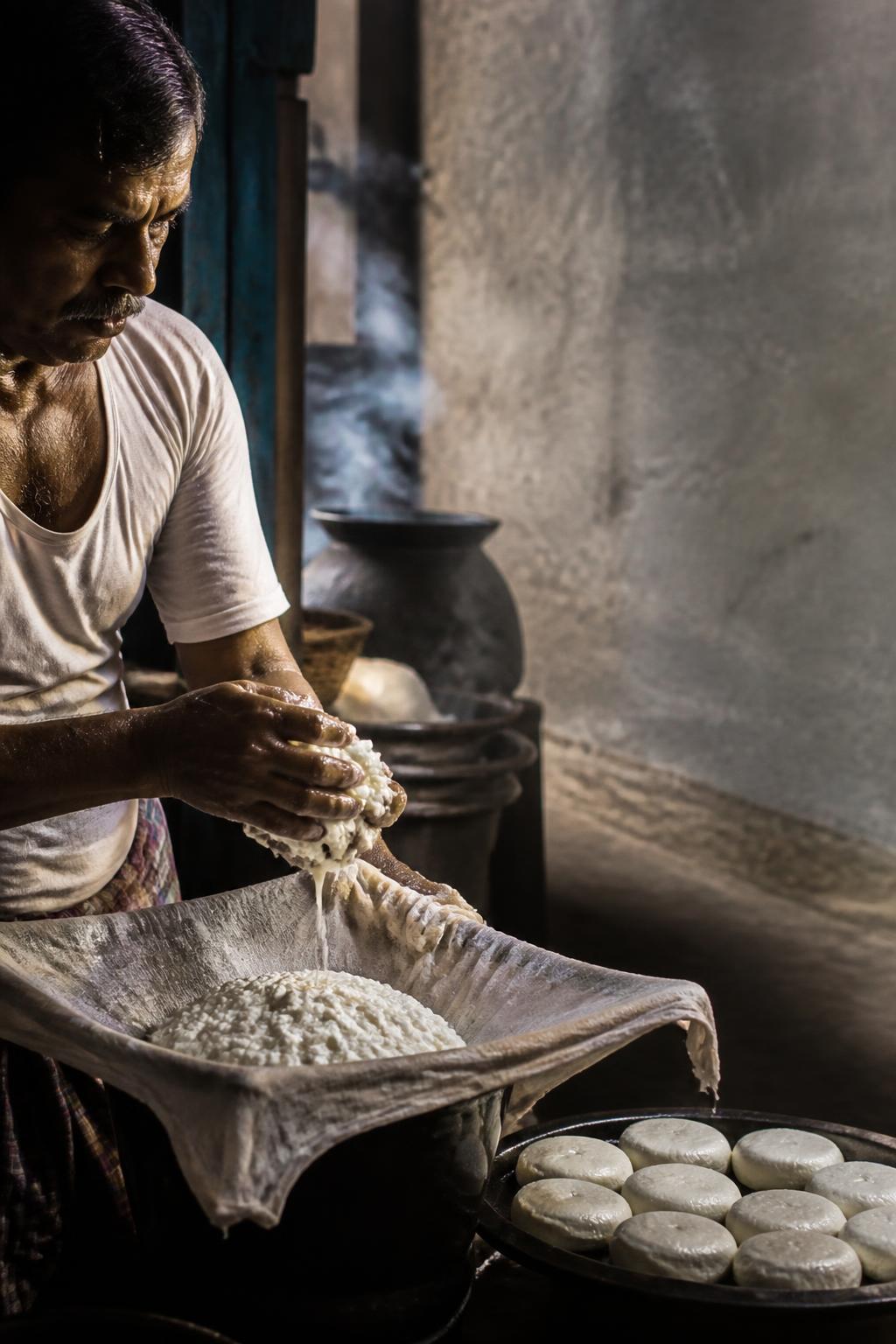 A cheesemaker drains and shapes fresh curds into small rounds.