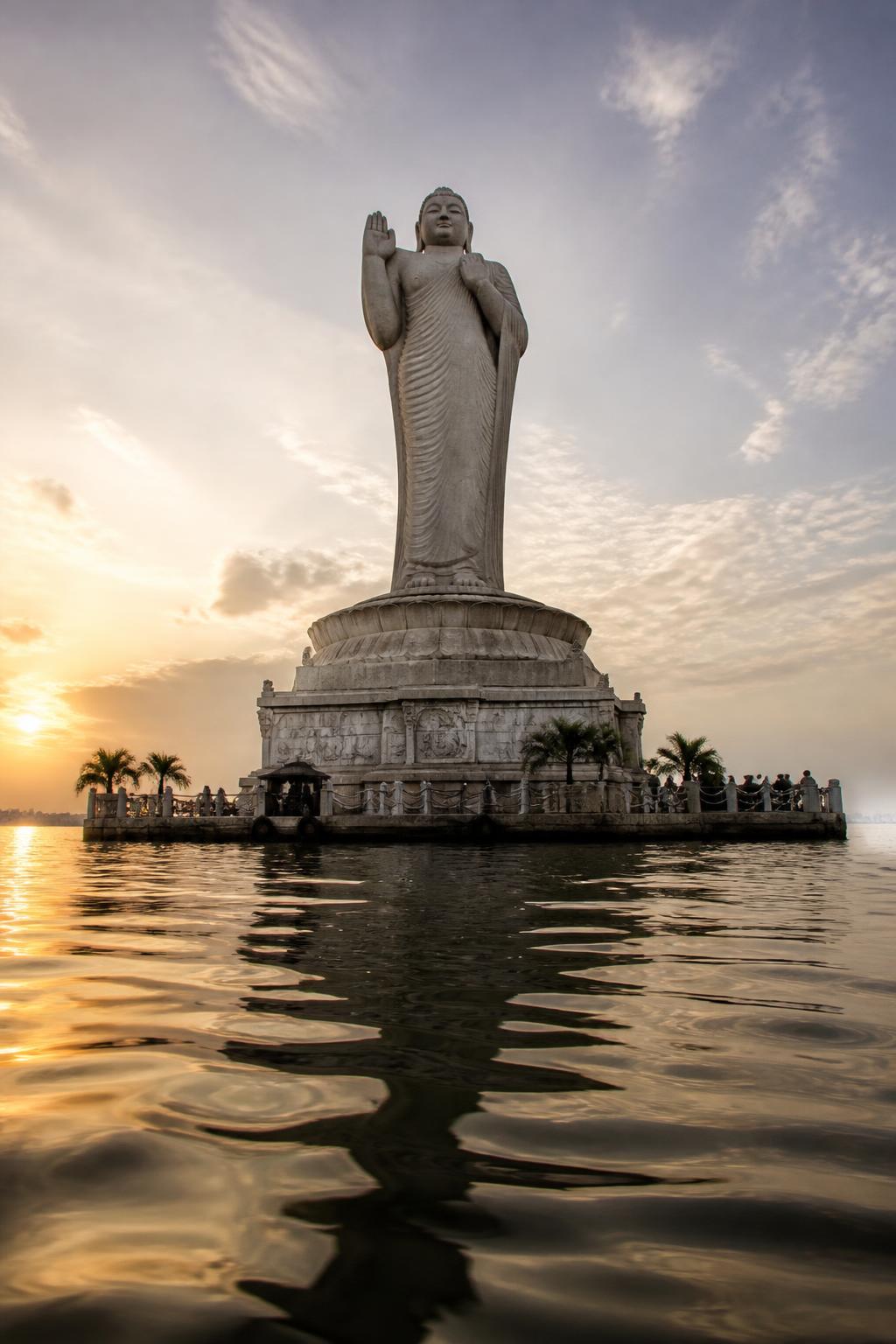 The Buddha statue rising from its rocky platform in Hussain Sagar at sunset.