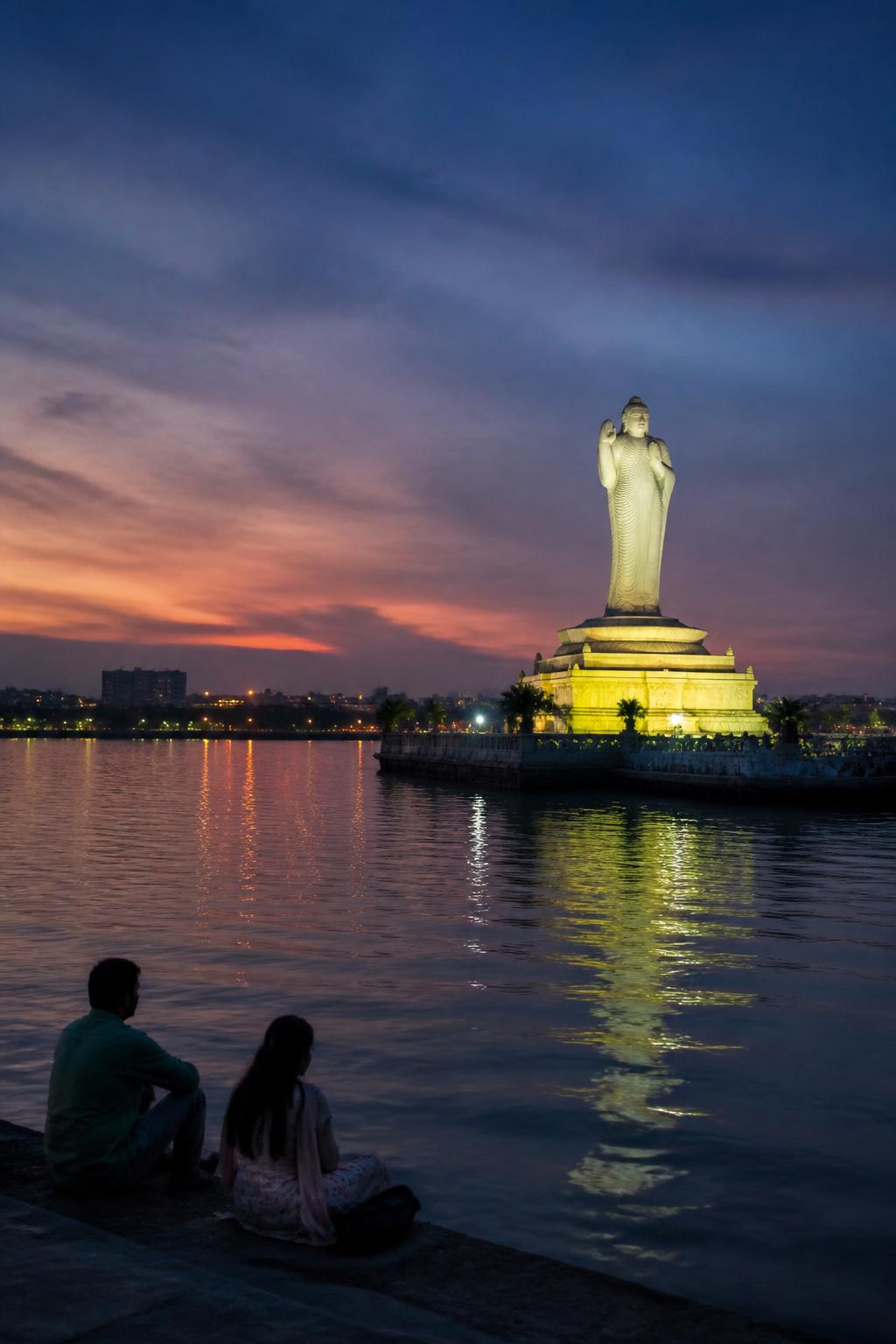 The illuminated Buddha statue reflected in Hussain Sagar with Hyderabad beyond.