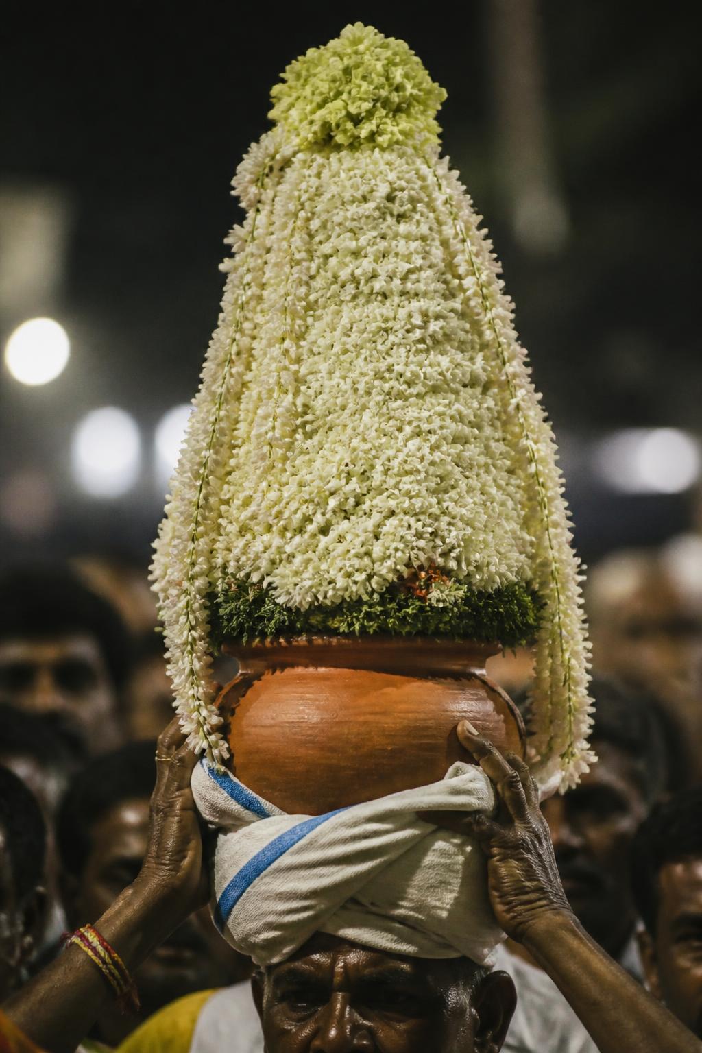 A tall jasmine-covered floral pyramid balanced on a mud pot.